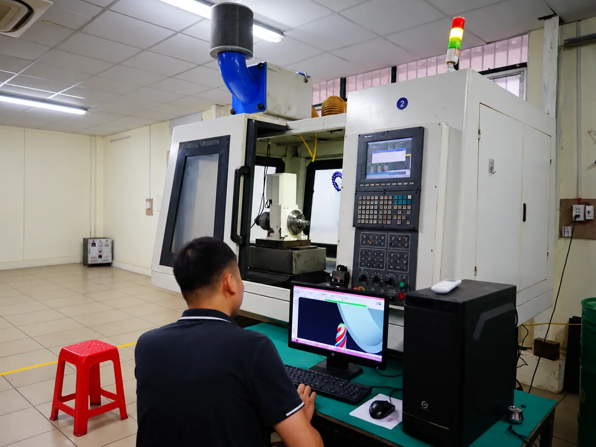 Engineer designing a special end mill on screen beside the CNC tool grinder