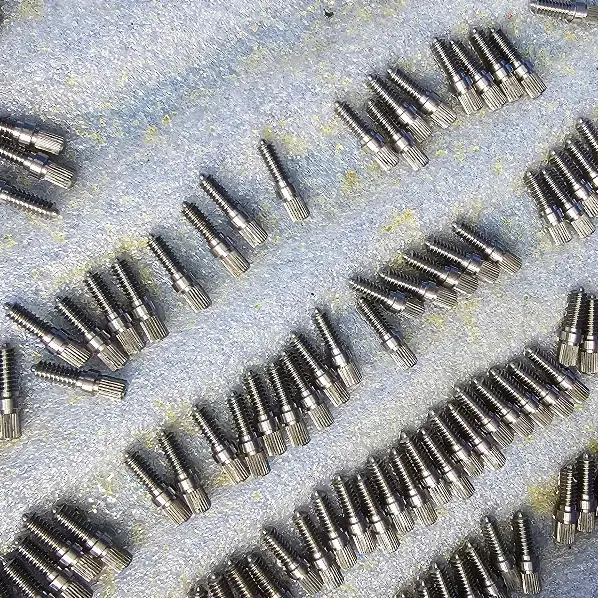Batch of small CNC turned threaded pins with shoulder laid out on foam